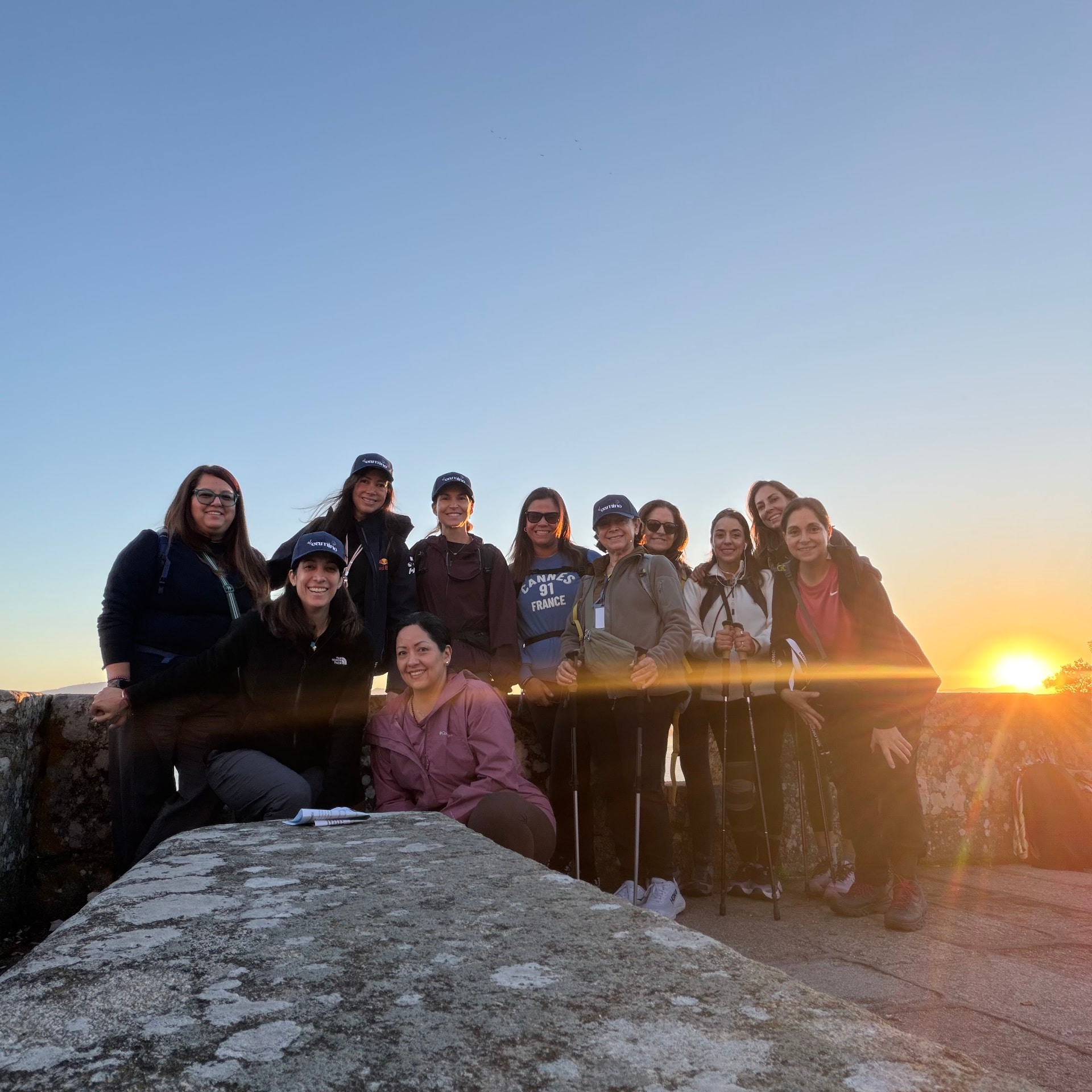 Grupo de mujeres del Camino reunidas junto a un muro de piedra al atardecer